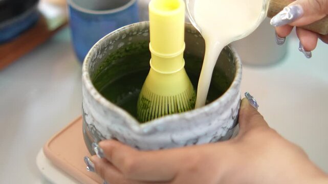 4K High angle view of barista using traditional bamboo whisk to mix green matcha tea powder in ceramic bowl, Japanese tea ceremony and healthy beverage concept.