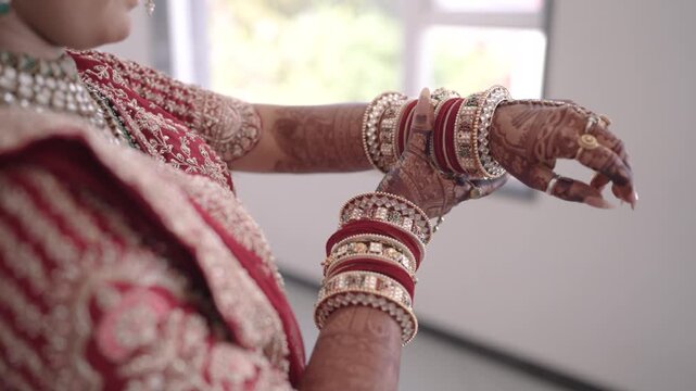 Close up of an Indian bride hands decorated with beautiful mehndi design, wearing traditional red and gold bangles with haathphool