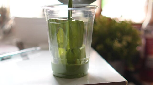 4K Close-up barista pouring concentrated green matcha tea into a plastic glass filled with ice cubes, Japanese cafe menus green tea marketing and healthy drink designs.