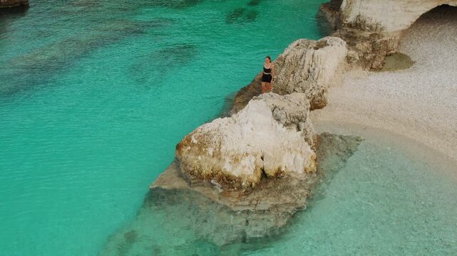 Woman walking alone along Fteri pebble beach by calm turquoise sea with caves in Kefalonia Greece