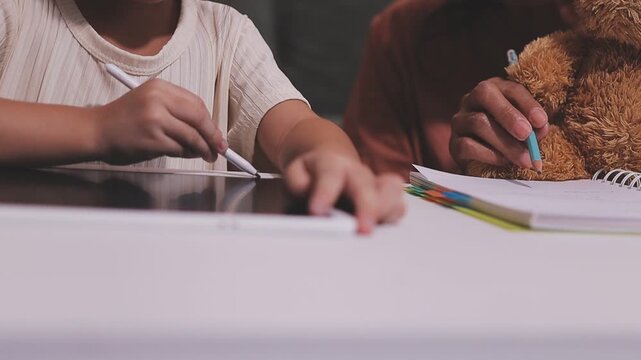 Small children hands hold wax crayons to draw rainbow on paper sheet. Diverse kids engage in creative craft activity together sitting on floor. Little students practice coloring skills at home school