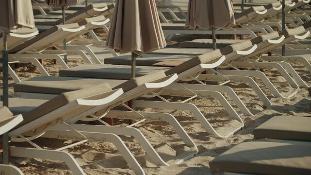 Empty beach lounge chairs with sunshades on a sandy beach, waiting for tourists to relax and enjoy summer vacation