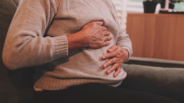 Stomach ache, cramps and hands of woman with abdomen pain due to constipation, menstruation or ibs issue. Sick, home and person suffering and holding belly in a house lounge, couch and living room