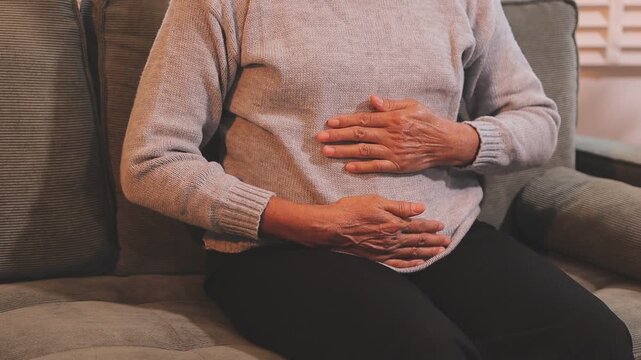 Stomach ache, cramps and hands of woman with abdomen pain due to constipation, menstruation or ibs issue. Sick, home and person suffering and holding belly in a house lounge, couch and living room