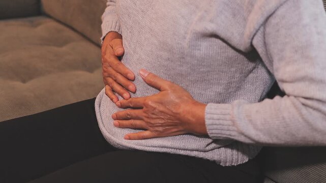 Stomach ache, cramps and hands of woman with abdomen pain due to constipation, menstruation or ibs issue. Sick, home and person suffering and holding belly in a house lounge, couch and living room