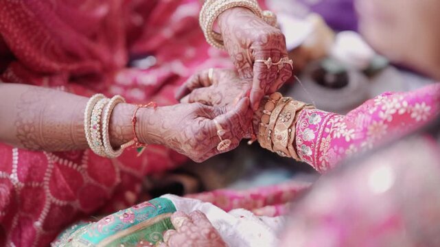 Close up of an Indian wedding ritual showing hands of two women with mehndi designs and traditional gold bangles