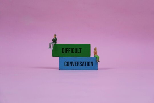 Difficult Conversation Concept With Miniature Couple Sitting on Stacked Blocks Against pink Background. illustrating relationship conflict and the need for dialogue or counseling.