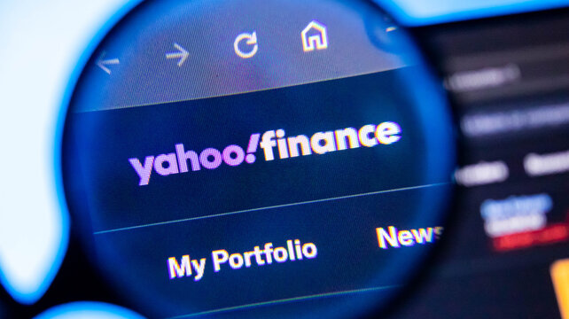 A close-up view of the yahoo finance website shown on a computer screen through a magnifying glass.