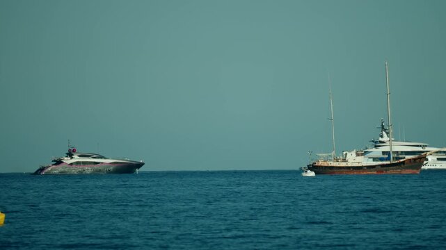 Two types of boats, a modern luxury yacht and a classic old sailing ship, coexist on the vast blue sea under a clear sky