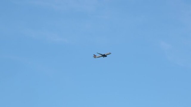 Camera pans with airline jet ascending past wispy clouds in blue sky
