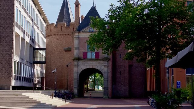 Smooth tracking shot reveals historic Sabelspoort city gate, ancient defense tower structure framed by trees and modern buildings on sunny summer day in Arnhem.
