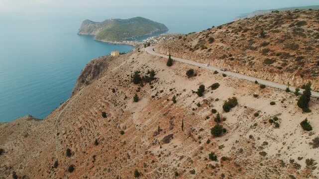 Coastal road with vehicles curving along rocky cliffs above calm blue sea on a clear sunny day in Kefalonia, Greece