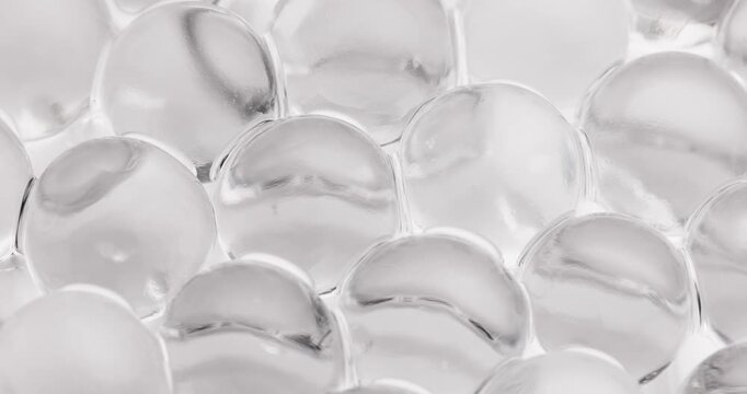 Slow motion macro of transparent hydrogel beads shifting and settling on white studio surface under soft light, concept experimental with microscope for cell structure.