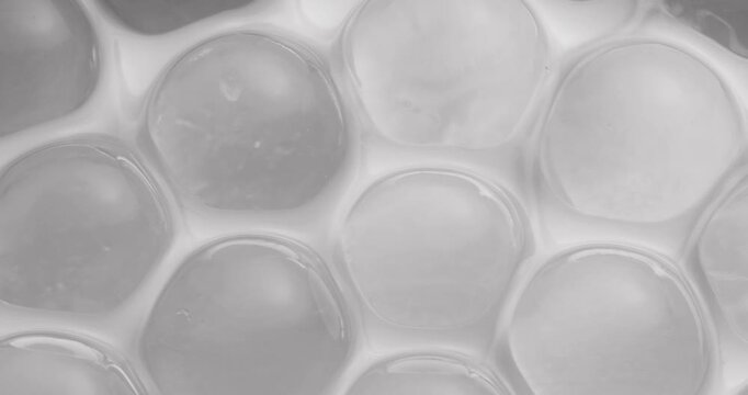 Slow motion macro of translucent gel beads shifting across honeycomb silicone surface in closeup, concept experimental with microscope for cell structure.