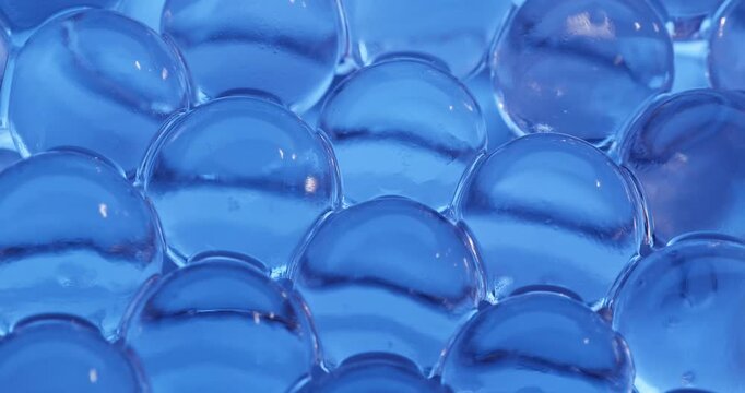Panning close up across blue hydrogel water beads clustered on reflective surface, concept experimental with microscope for cell structure.