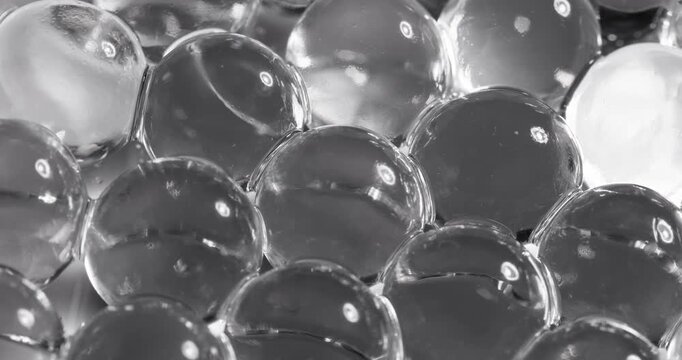 Slow motion glass marbles shifting and settling in tight macro cluster on reflective tabletop surface under studio lighting, concept microscope for cell structure.