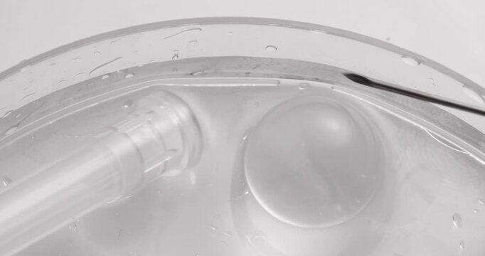 Slow motion needle piercing clear droplet on glass petri dish in laboratory closeup tracking shot.