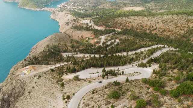 Winding coastal road with moving cars above bay in Kefalonia, Greece on a clear summer day