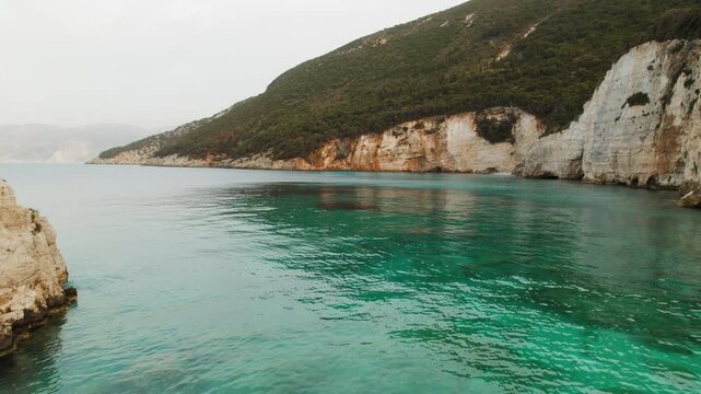 Steep coastal cliffs rising above calm turquoise sea water on an overcast day