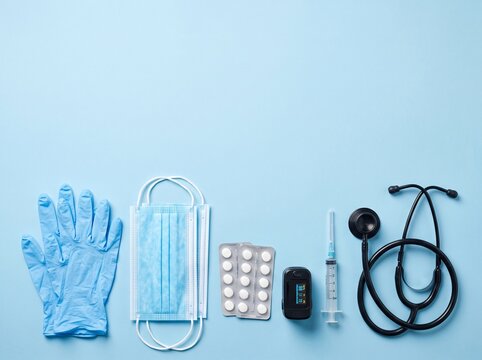 Medical Clipboard with Stethoscope, Masks, Gloves, Pills and Syringe on Blue Background in Slightly Irregular Flat Lay Composition with  Copy Space