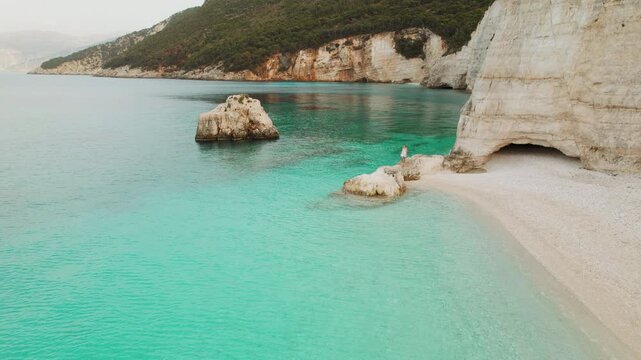 Secluded Kefalonia bay with white cliffs emerald water and tiny figure of woman walking and enjoying nature, Greece