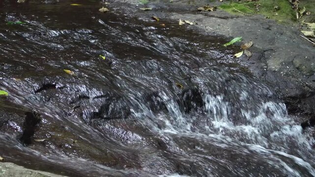 Close up shot of clear mountain river water flowing rapidly over dark rocks at Dholo Waterfall, Indonesia, representing pure freshwater resources and environmental sustainability.