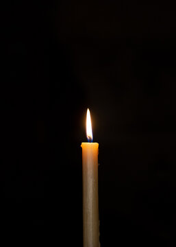 Single lit wax candle flame in the dark, symbolic of hope and faith, religious ritual element.