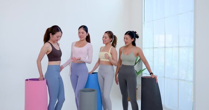 Asian female friends stand beside yoga mat, exchanging cheerful high five after class, celebrating fitness progress, wellness support, body confidence, bright studio community lifestyle together.