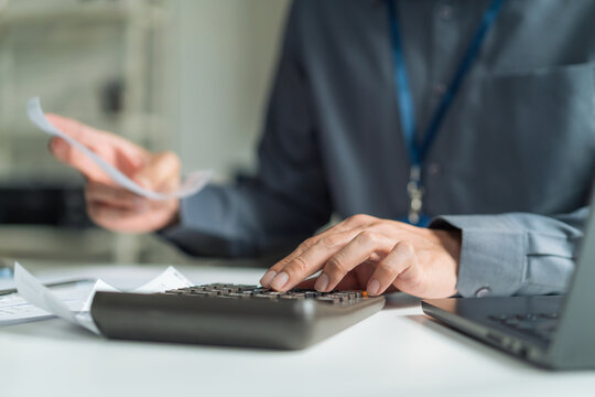 Close-up of accountant using calculator while checking financial bills and receipts at office desk.