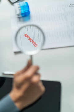 Close-up through magnifying glass of red approved word stamped on business document contract.