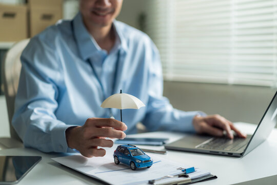 Close-up of insurance agent hand holding small umbrella over toy car for auto insurance and vehicle protection concept.