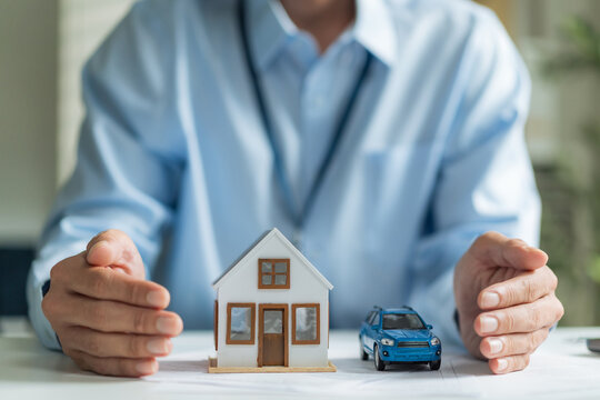 Close-up of businessman hands protecting house model and toy car for real estate and auto insurance concept.