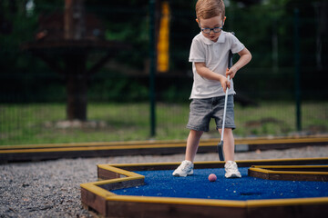 Obraz premium Boy playing mini golf with concentration outdoors