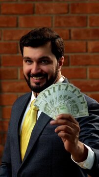 Indian businessman flaunting money hand fan made of five hundred rupee notes in cozy office setup. Asian CEO or entrepreneur in formal attire holding INR cash fan with beard against red brick wall
