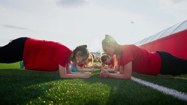 Focused womens soccer team holding core plank positions on sunny outdoor training field, building strength, stability, and unity during pre-season conditioning drills