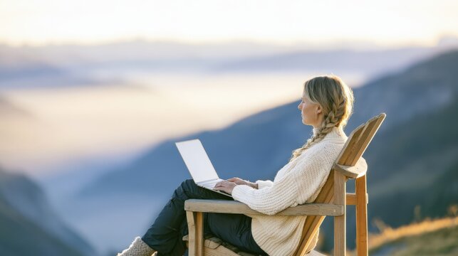 Young woman with braided hair in cream sweater using laptop while sitting in Adirondack chair outdoors