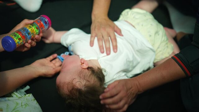 Toddler receiving pediatric physical therapy for developmental exercise, therapist assisting movement with colorful rattle toy