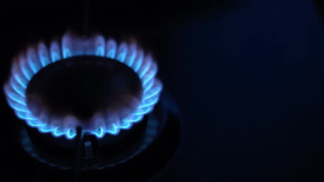 Close-up of a bright blue natural gas flame flickering on a kitchen stove burner in the dark