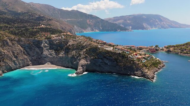 Wide 4K aerial shot revealing the Assos peninsula bay with anchored boats and turquoise waters under a clear blue sky in Kefalonia Island, Greece