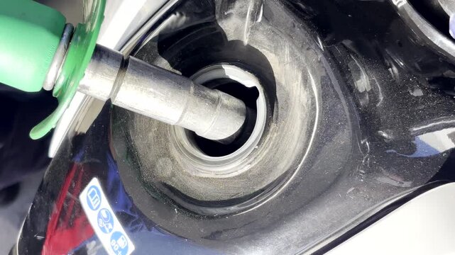 Closeup of fuel pump nozzle inserted into motorcycle tank to fill up with petrol
