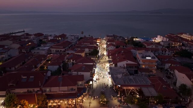 Pefkohori new town road leading to Pefkochori beach seaside promenade at night with traditional greek tavernas, beach bars, nightclubs, Halkidiki, Aegean Sea, Drone shot