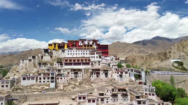 Drone arc shot orbiting the historic and colorful Likir Monastery complex built on a rocky hillside against desert mountains in Leh Ladakh, India.