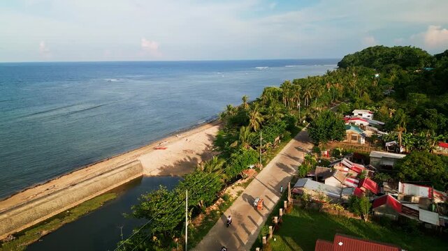 Orbiting aerial drone shot of coastal barangay village with coconut groves, beach road, and rural homes - Igang, Virac, Catanduanes, Philippines