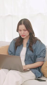 Tired young Asian woman closing her laptop, rubbing her eyes, and stretching after working from home.