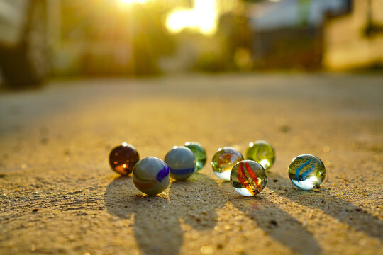 Colorful glass marbles scattered on a sandy path during the golden hour sunset with warm light and soft shadows
