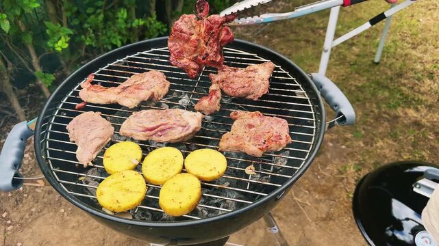 Meat and potatoes are grilled over a fire. The cook turns the pieces of meat on the grill. Backyard BBQ. High quality 4k footage
