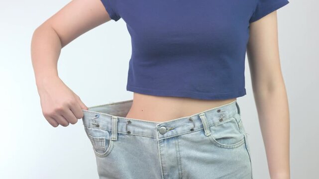 Proud confident happy woman showcases successful healthy weight loss journey pulling loose denim trouser to display slim waist fitness progress