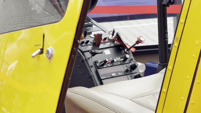 Close view of a yellow aircraft cockpit with open door, showing control panel, levers and a light seat inside a small plane.