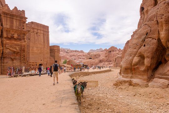 Tourists pass Bedouin markets, rock tombs and caves on the sandy Siq path through the Street of Facades in the ancient city of Petra, Jordan.