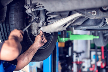Selective focus to hands of professional mechanic using a wrench tool to repair and adjust car rear suspension system in auto service shop. © Koonsiri